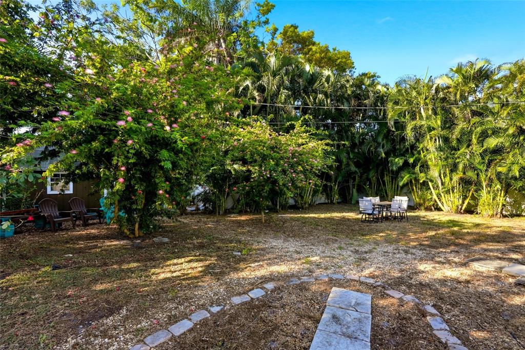 A backyard features a gravel area, a stone path, patio furniture, and lush tropical trees — 220 45TH AVENUE S, ST PETERSBURG, FL