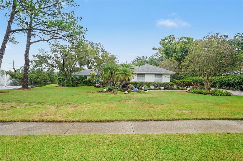 An aerial view shows a house with a gray roof situated behind a pond fountain — 2950 ST ANDREWS BOULEVARD, TARPON SPRINGS, FL