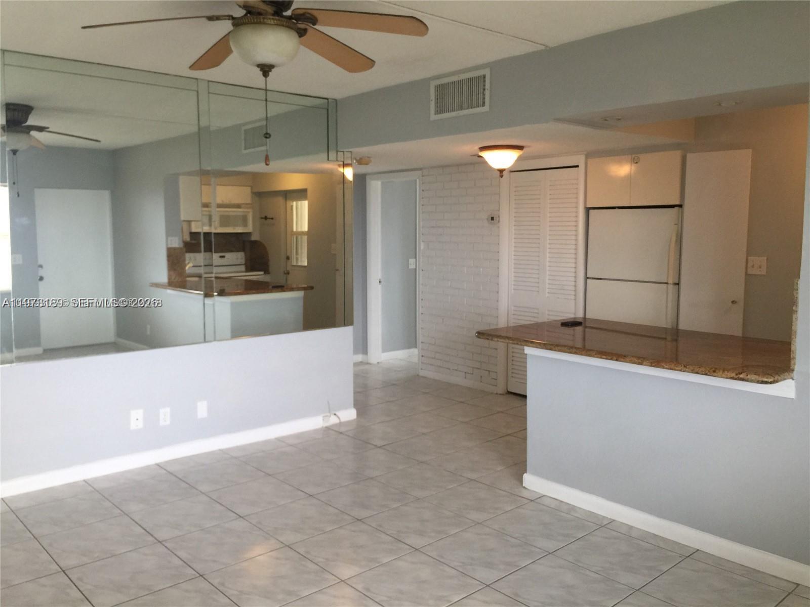 A living room with tiled floors, a mirrored wall, and a kitchen breakfast bar — 901 S Surf Rd # 402, Hollywood FL 33019, HOLLYWOOD, FL