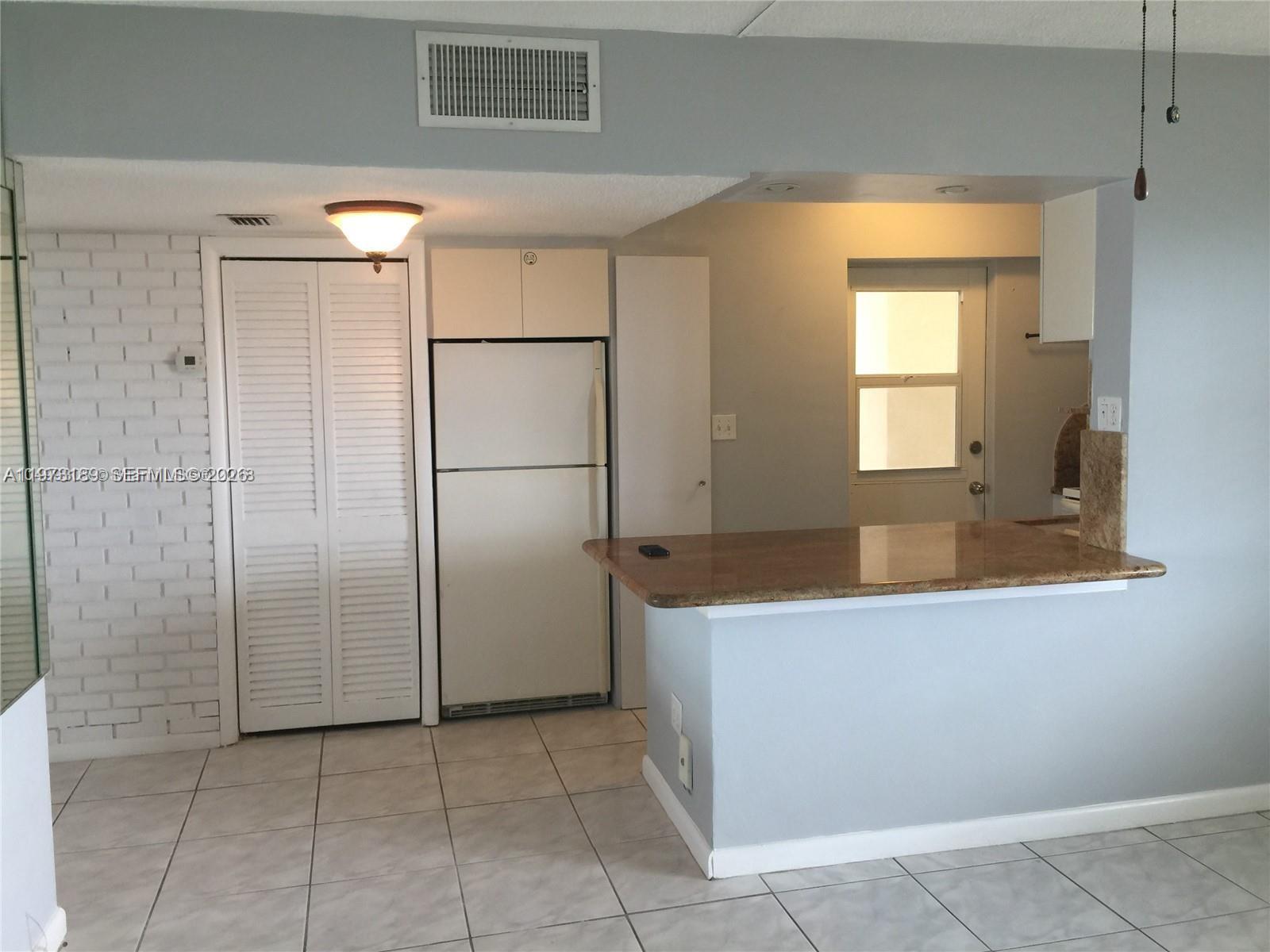 A kitchen area features a white refrigerator, a granite breakfast bar, and tiled flooring — 901 S Surf Rd # 402, Hollywood FL 33019, HOLLYWOOD, FL
