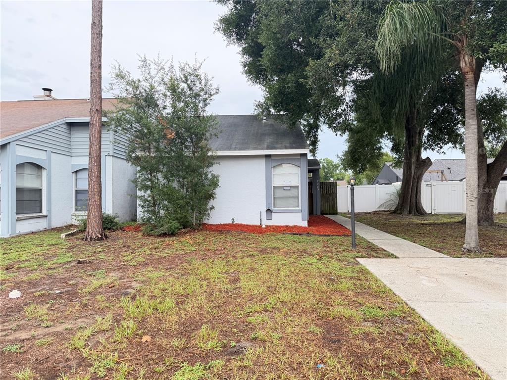 A single-story house with a white exterior, gray trim, and a front yard with trees — 7705 CITRONELLA COURT, TAMPA, FL