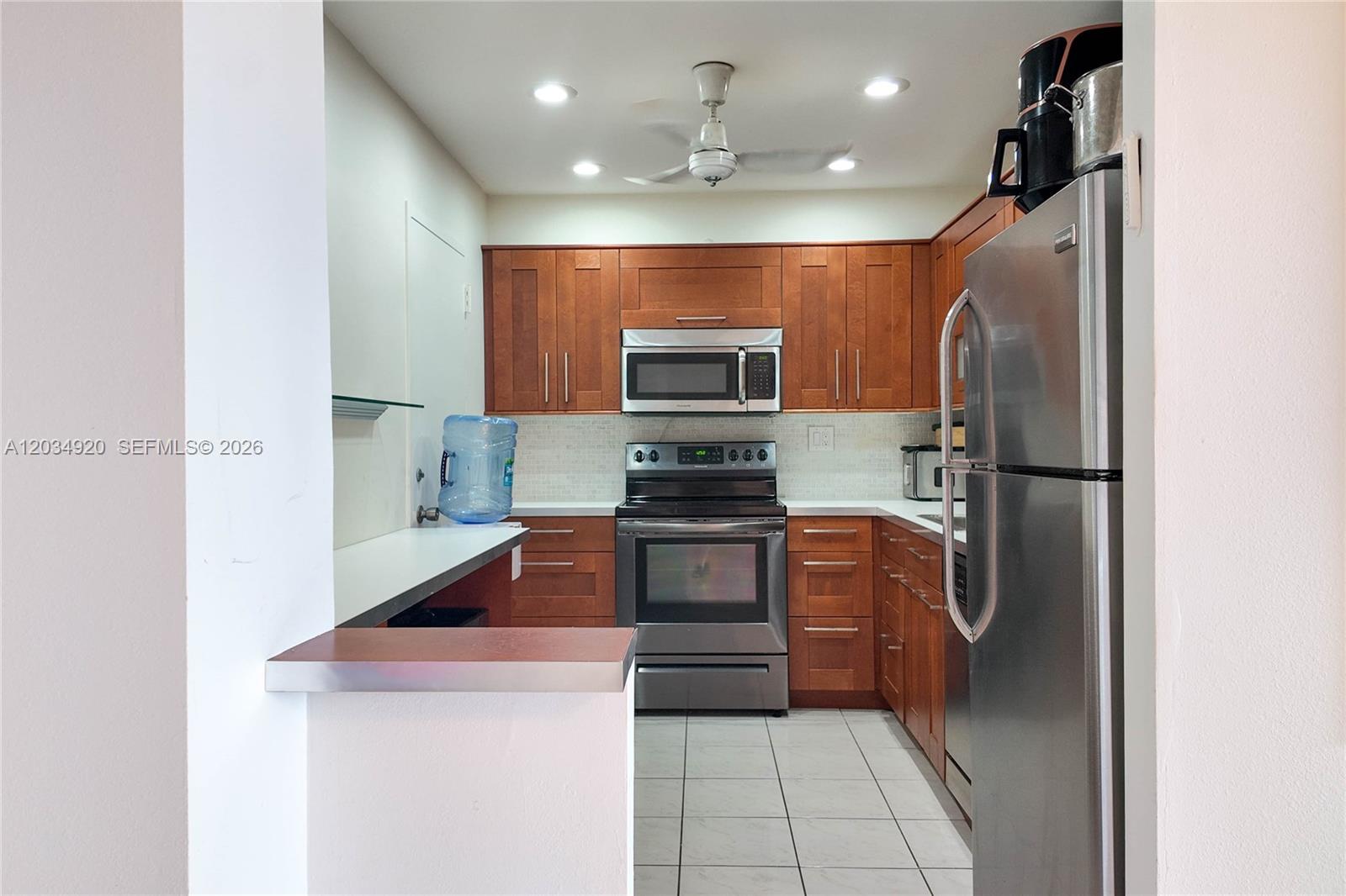 A kitchen features wood cabinets, stainless steel appliances, white countertops, and a ceiling fan — 1950 S Ocean Dr # 5B, Hallandale Beach FL 33009, HALLANDALE BEACH, FL