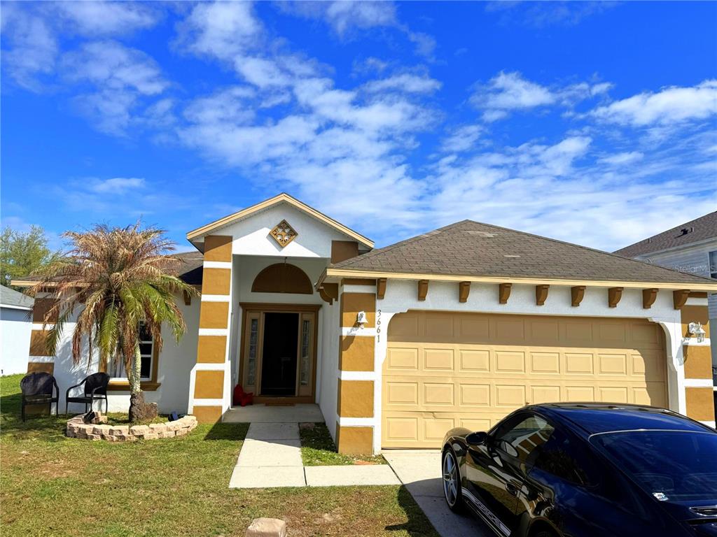 A single-story house with a tan garage, white stucco walls, and brown decorative corner accents — 3661 QUEENS COVE BOULEVARD, WINTER HAVEN, FL