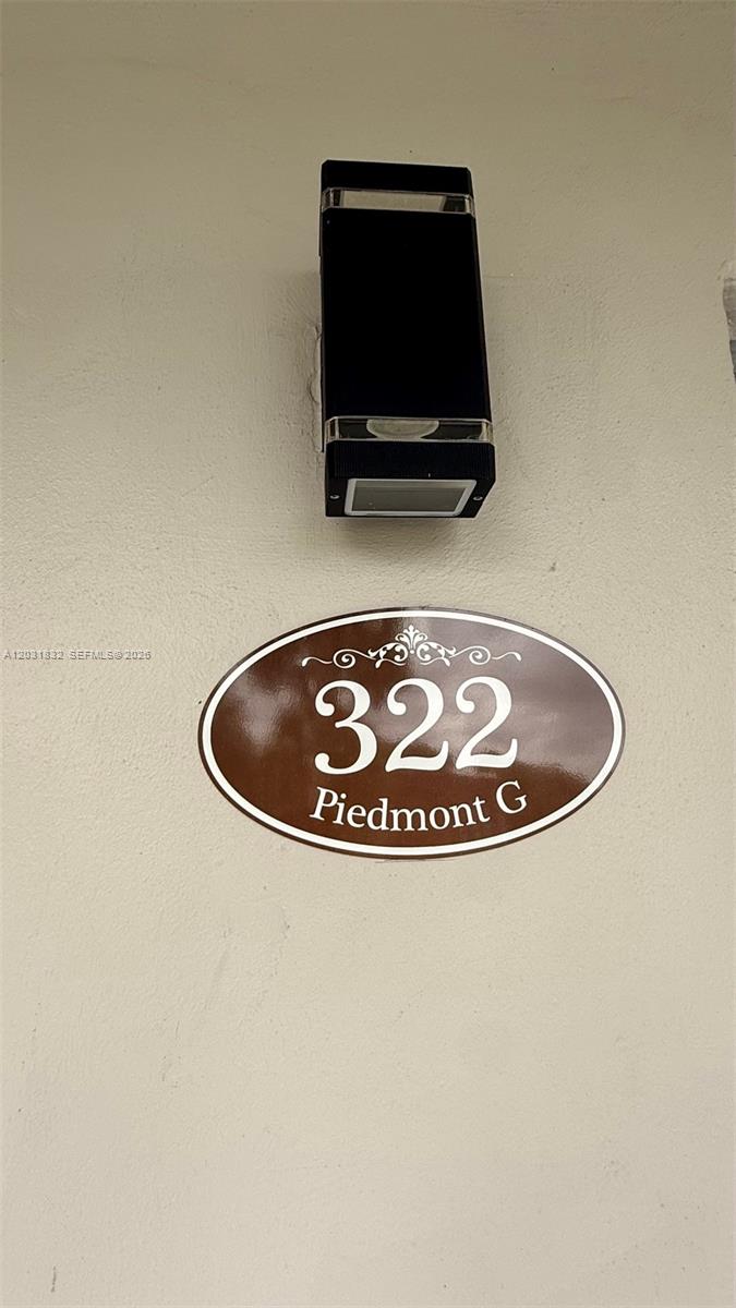 A wall-mounted outdoor light fixture is positioned above an oval address plaque reading 322 Piedmont G — 322 Piedmont G # G, Delray Beach FL 33484, DELRAY BEACH, FL