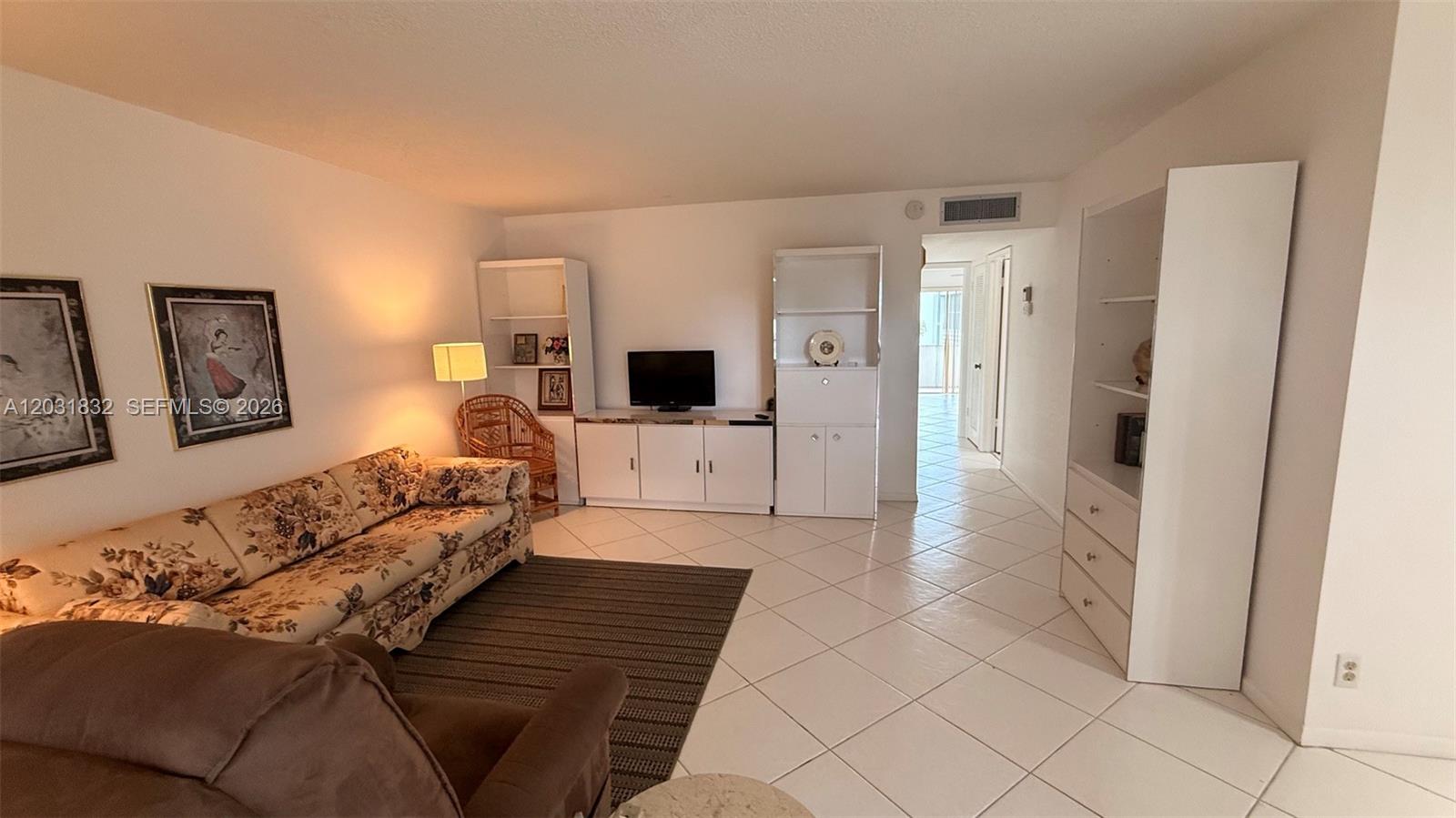 A living room features a floral sofa, tiled floors, white cabinetry, and wall art — 322 Piedmont G # G, Delray Beach FL 33484, DELRAY BEACH, FL