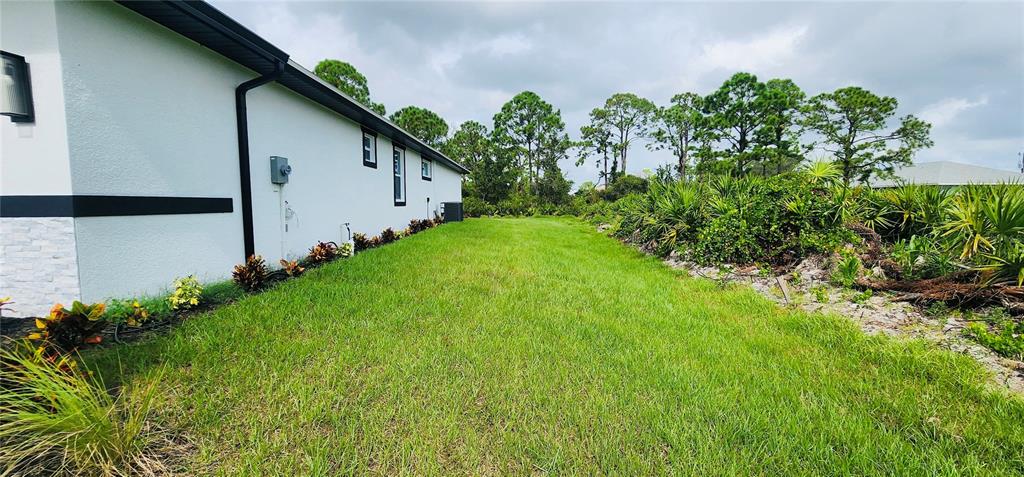 The side exterior of a white house features black trim and a grassy yard — 5555 VERACRUZ TERRACE, PORT CHARLOTTE, FL