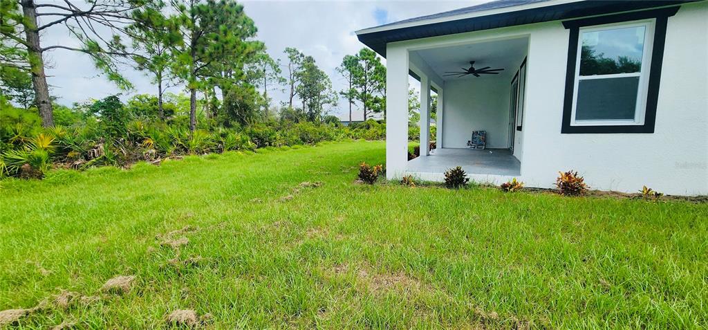 A white house with a covered patio overlooks a grassy backyard and wooded area — 5555 VERACRUZ TERRACE, PORT CHARLOTTE, FL