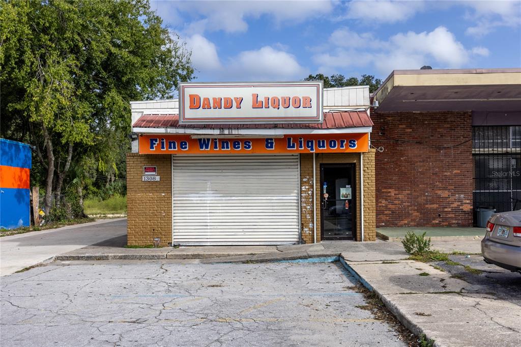 The exterior of a liquor store features a roll-down security gate and brick facade — 1308 E UNIVERSITY AVENUE, GAINESVILLE, FL