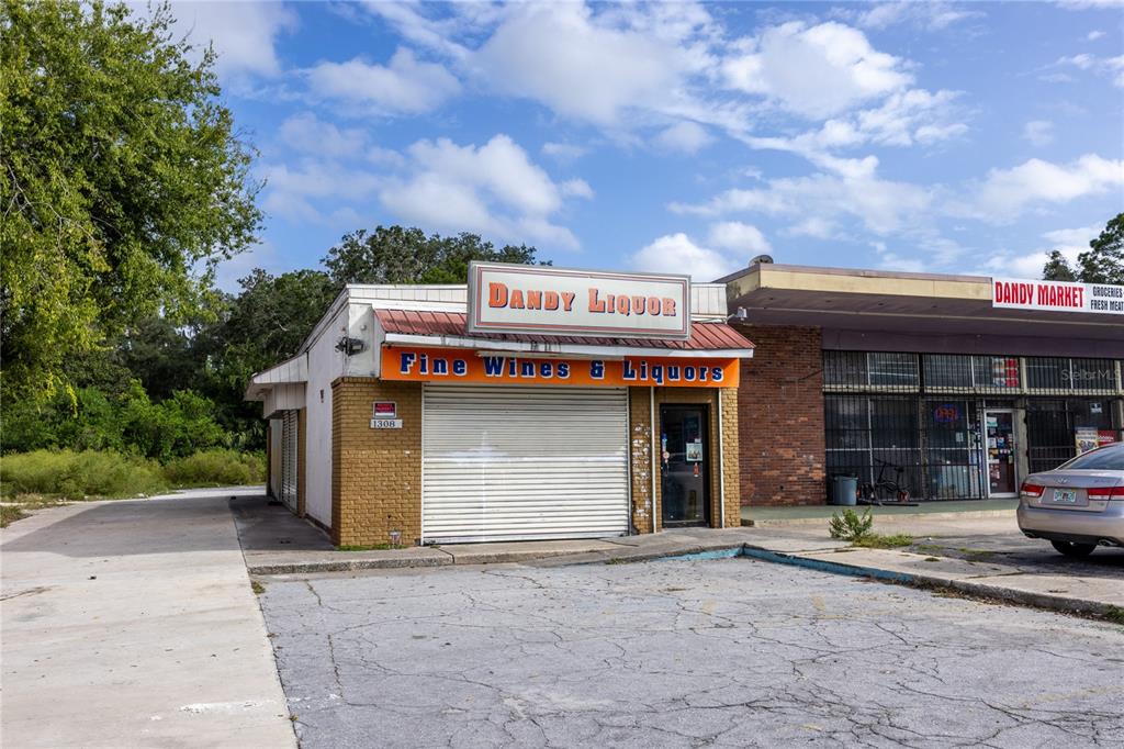 An exterior view of a small brick liquor store and adjacent market with a parking lot — 1308 E UNIVERSITY AVENUE, GAINESVILLE, FL