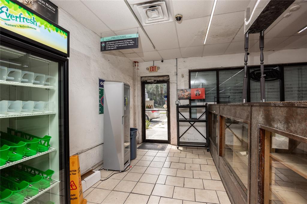 A commercial interior features a glass-door refrigerator, a tiled floor, and an exit door — 1308 E UNIVERSITY AVENUE, GAINESVILLE, FL