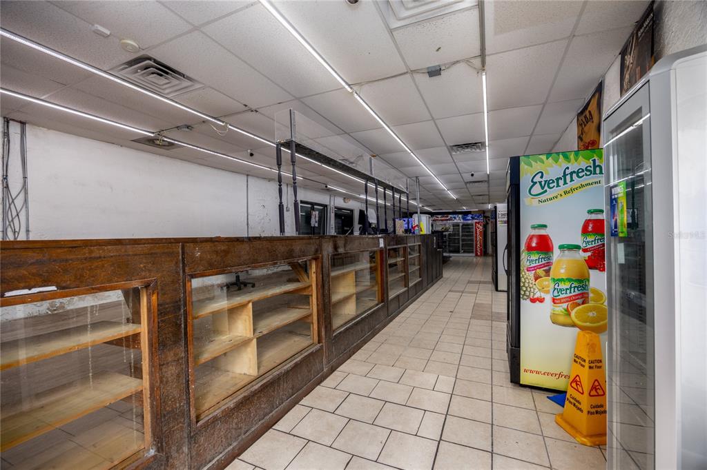 A commercial interior features a long wooden display counter and a beverage cooler — 1308 E UNIVERSITY AVENUE, GAINESVILLE, FL