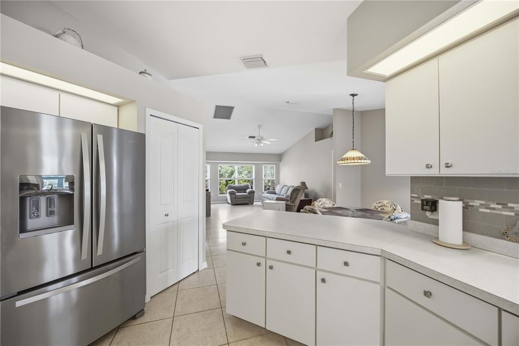 A kitchen with white cabinets and stainless steel appliances overlooks an open-concept living area — 15608 MELPORT CIRCLE, PORT CHARLOTTE, FL