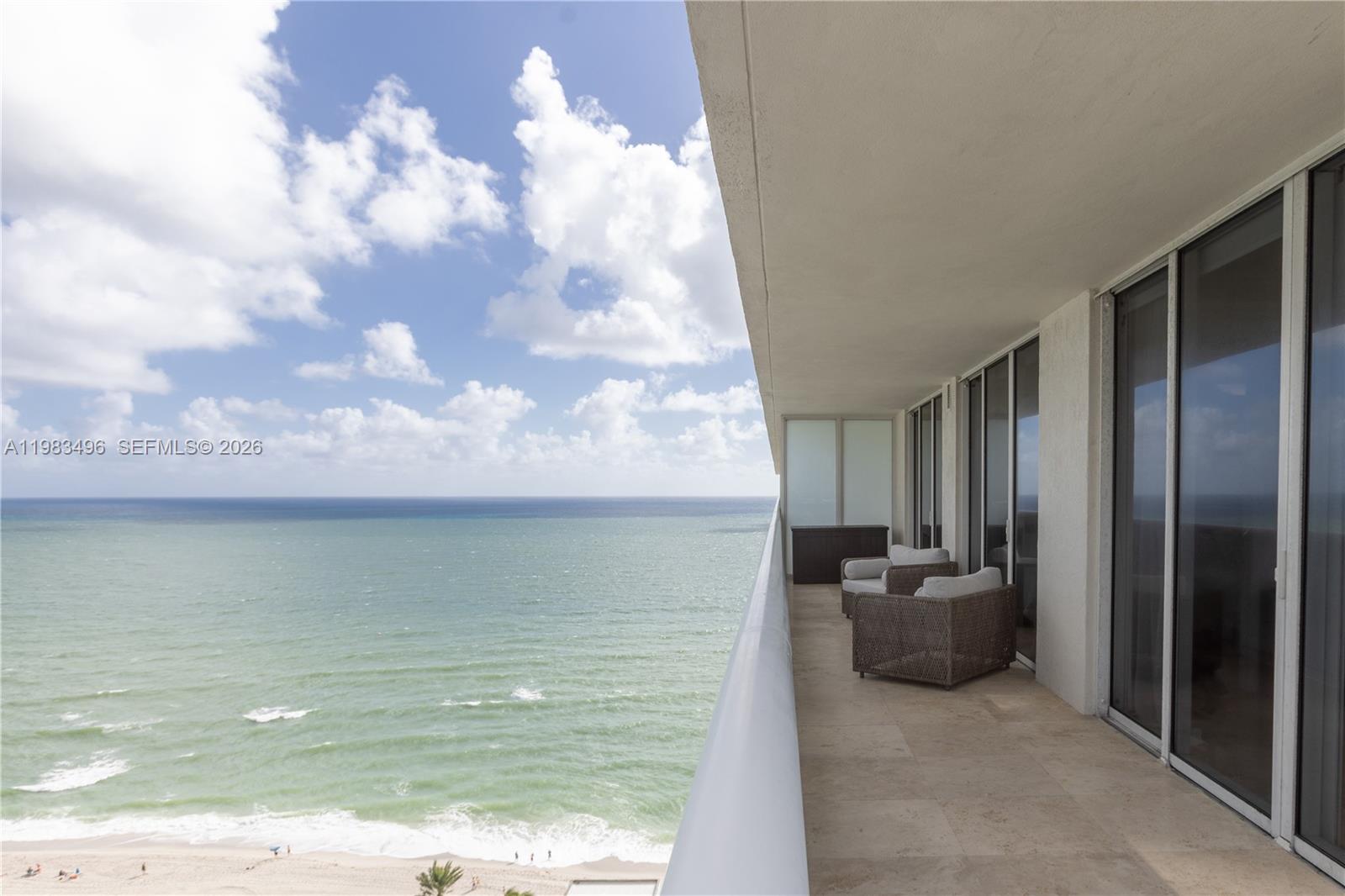A balcony with two wicker chairs overlooks the ocean under a cloudy blue sky — 1830 S Ocean Dr # 2108, Hallandale Beach FL 33009, HALLANDALE BEACH, FL