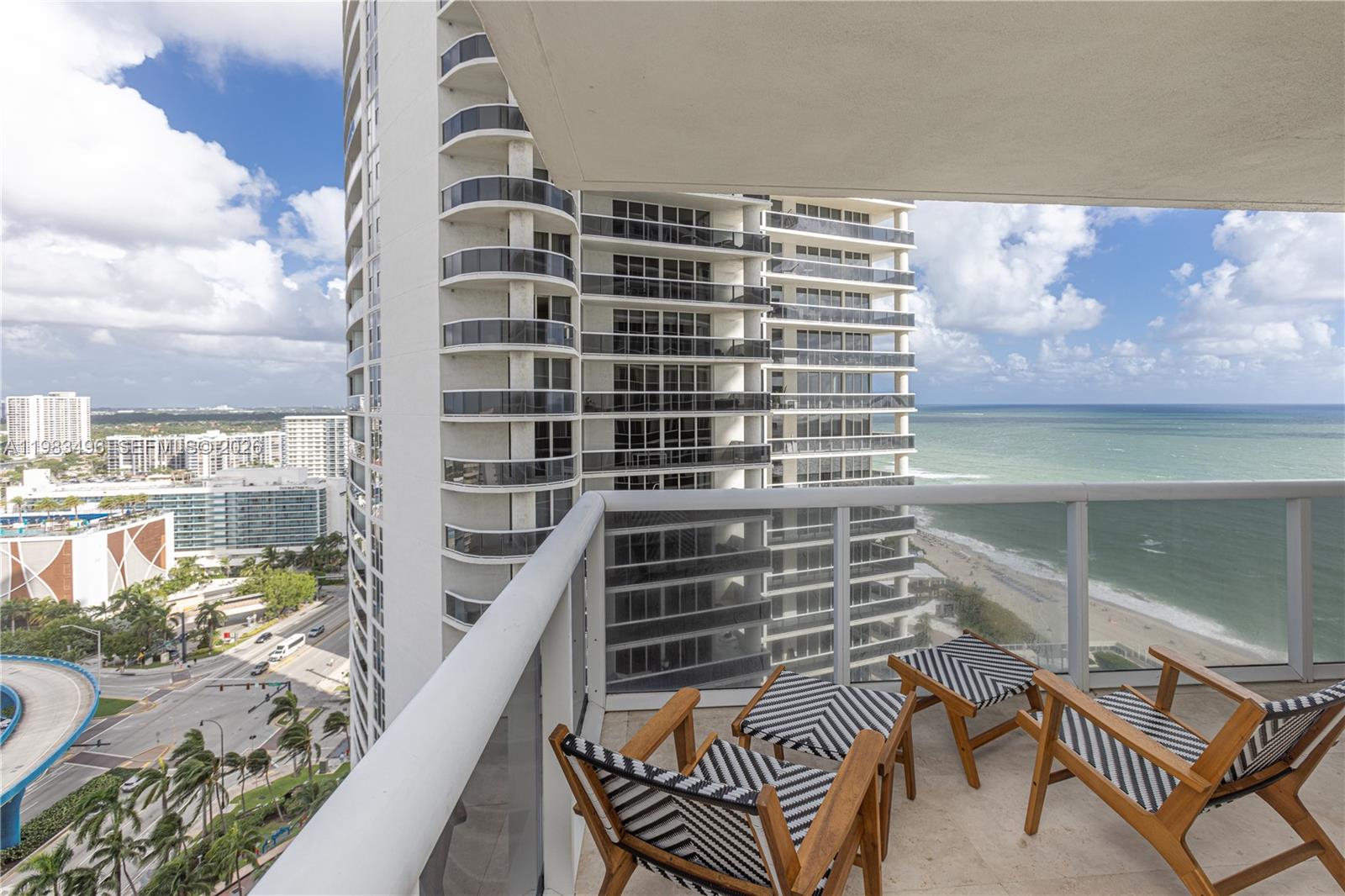 A high-rise balcony features two wooden chairs with black and white striped cushions overlooking the ocean — 1830 S Ocean Dr # 2108, Hallandale Beach FL 33009, HALLANDALE BEACH, FL