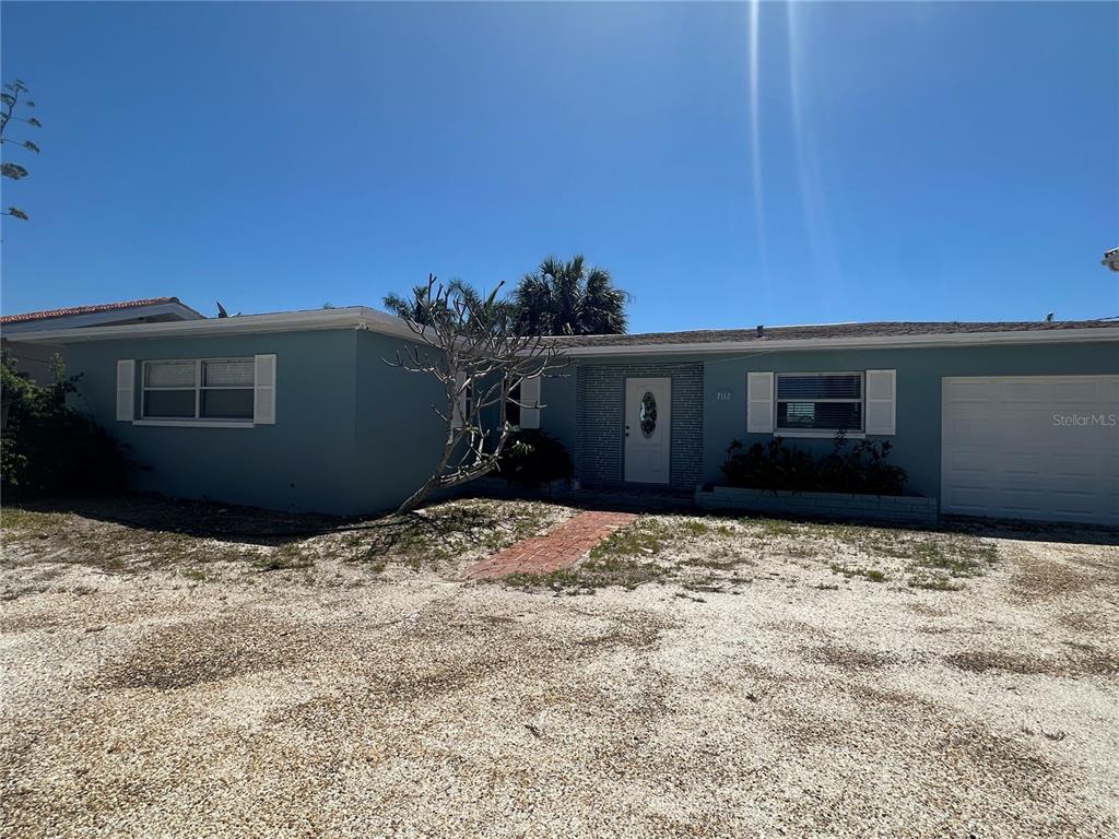 A single-story house with blue siding, a white garage door, and a gravel front yard — 7112 S SHORE DRIVE S, SOUTH PASADENA, FL