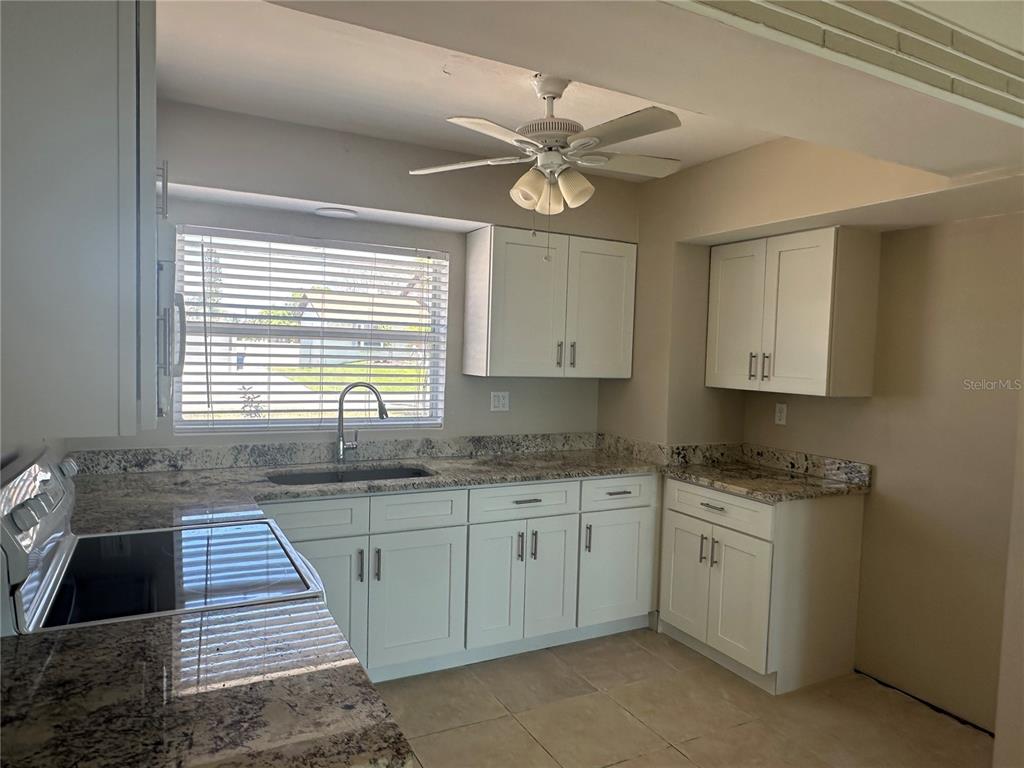 A kitchen features white cabinets, granite countertops, a ceiling fan, and a window with blinds — 7112 S SHORE DRIVE S, SOUTH PASADENA, FL