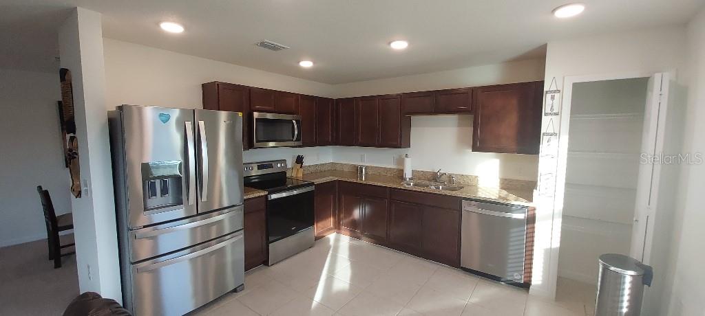 A kitchen features dark wood cabinets, stainless steel appliances, and beige granite countertops — 444 PATRICIA ALFORD DRIVE, HAINES CITY, FL