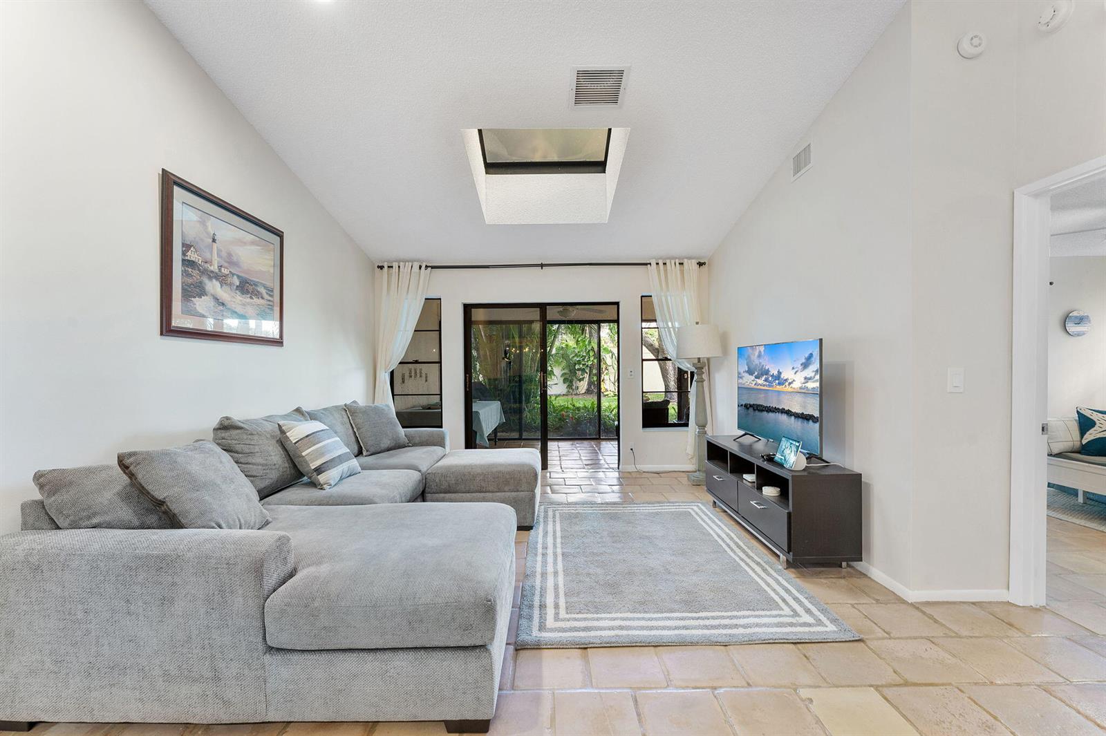 A living room features a gray sectional sofa, a television, a skylight, and tile flooring — 5861 Sunswept Lane # B, Boynton Beach FL 33437, BOYNTON BEACH, FL