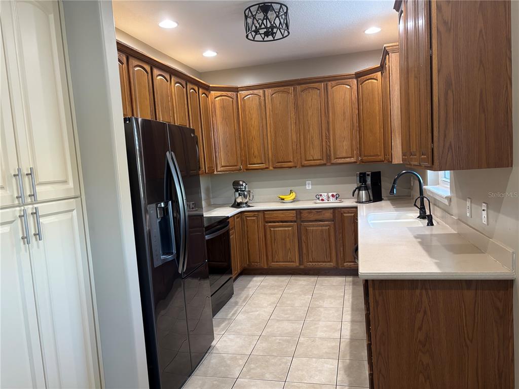 A kitchen features wood cabinets, a black refrigerator, a white countertop, and tile flooring — 152 NAUTICA MILE DRIVE, CLERMONT, FL