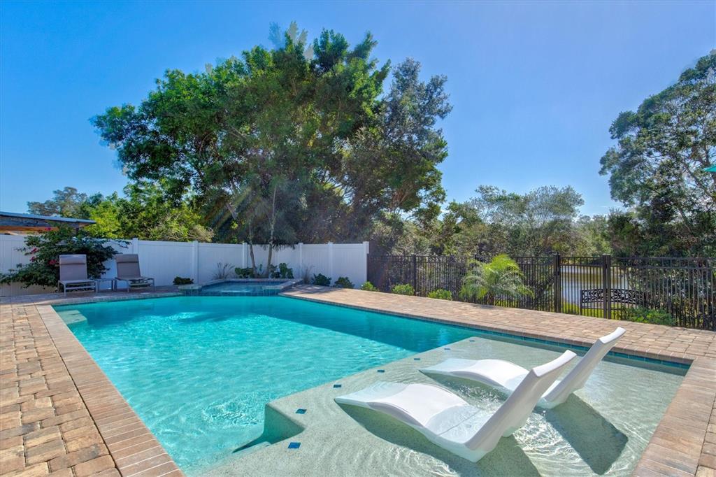 A swimming pool with a tanning ledge and lounge chairs sits in a fenced backyard — 3210 WOOD STREET, SARASOTA, FL