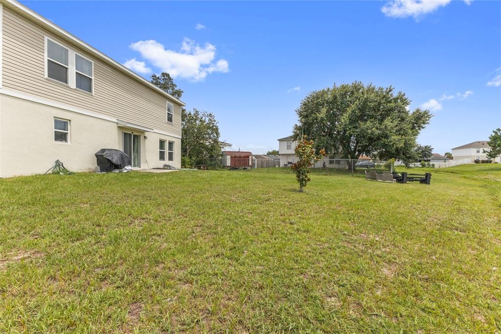 A grassy backyard behind a two-story house with beige siding and a small patio — 1889 SNAPPER DRIVE, POINCIANA, FL