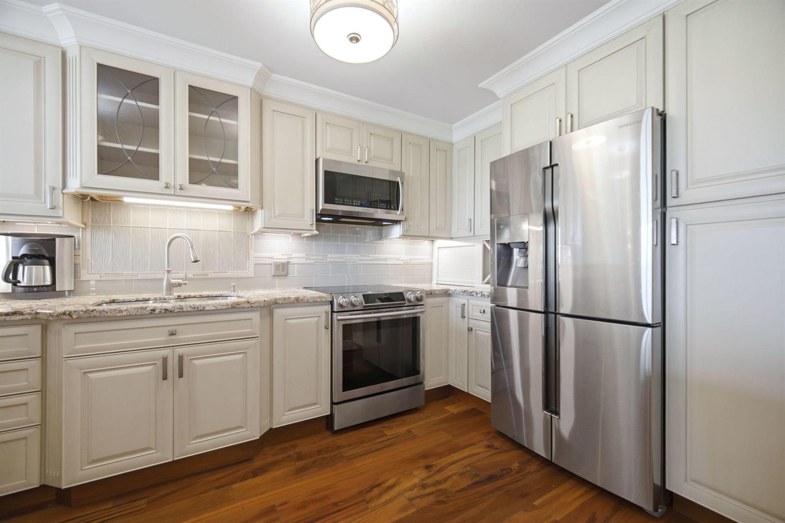 A kitchen features cream-colored cabinets, stainless steel appliances, granite countertops, and hardwood flooring — 2901 S Palm Aire Drive, Pompano Beach FL 33069, POMPANO BEACH, FL