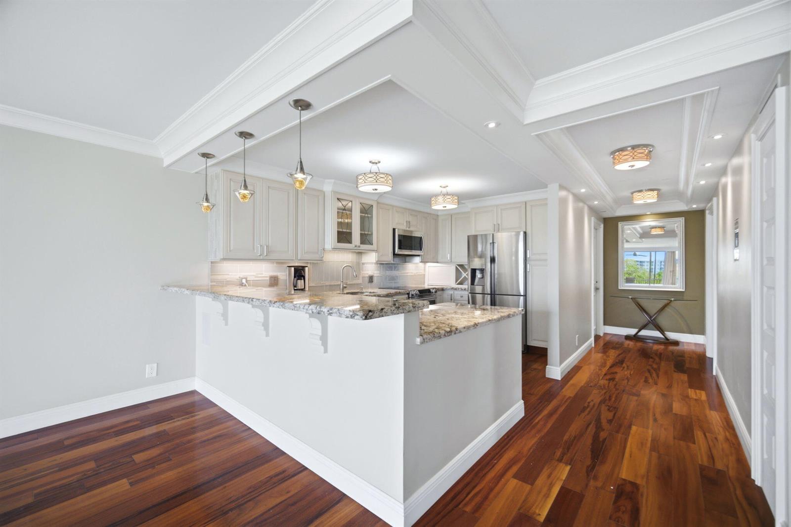A kitchen with granite countertops, light cabinetry, and hardwood floors features a breakfast bar island — 2901 S Palm Aire Drive, Pompano Beach FL 33069, POMPANO BEACH, FL