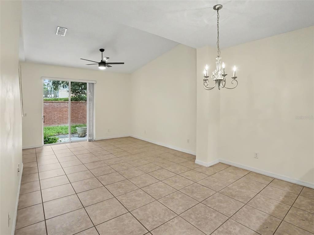 An empty room with beige tile flooring, a ceiling fan, a chandelier, and sliding glass doors — 1114 LIMESTONE RUN, SANFORD, FL