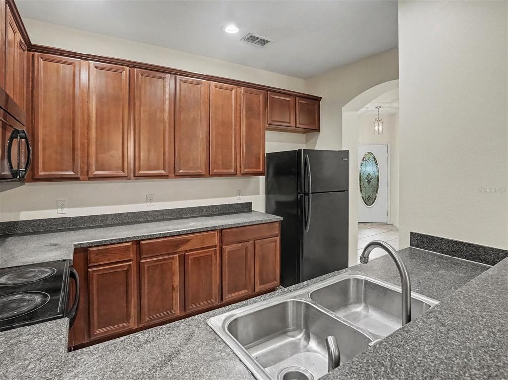 A kitchen features dark wood cabinets, black appliances, and gray speckled laminate countertops — 1114 LIMESTONE RUN, SANFORD, FL