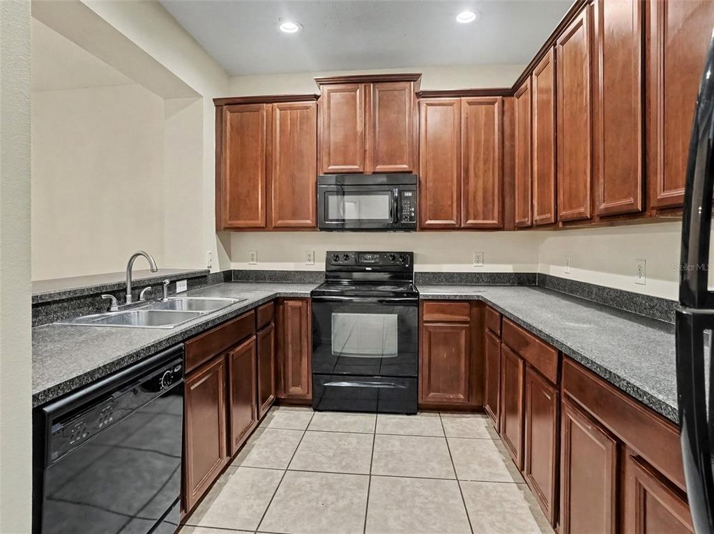 A kitchen with dark wood cabinets, black appliances, and gray speckled countertops — 1114 LIMESTONE RUN, SANFORD, FL