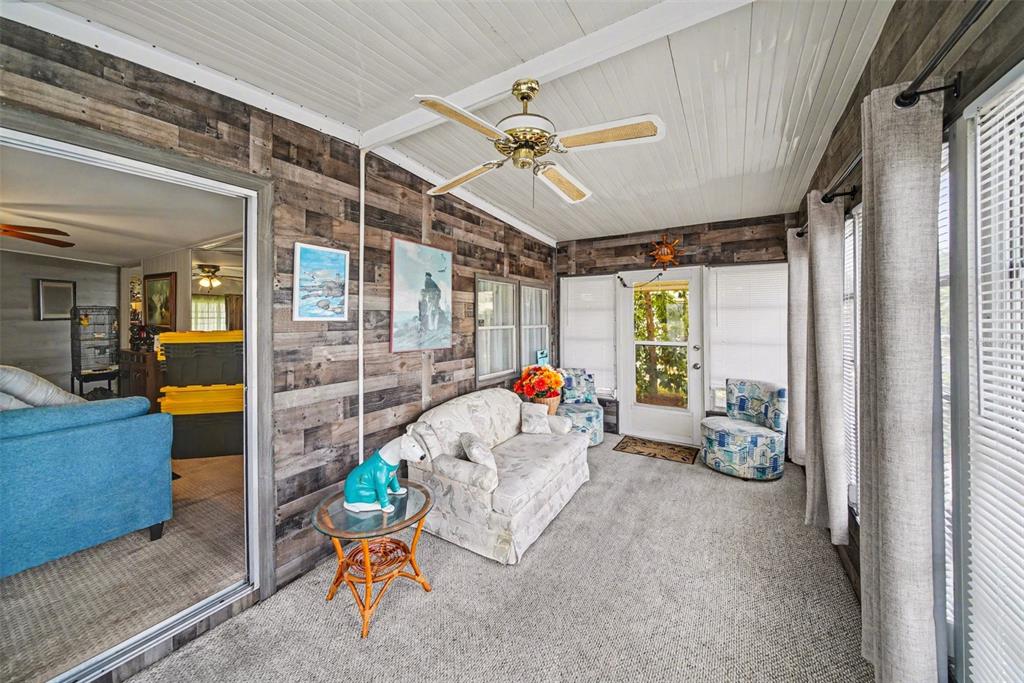 A sunroom features wood-plank walls, a ceiling fan, carpeted flooring, and a glass sliding door — 12501 ULMERTON ROAD UNIT 33, LARGO, FL