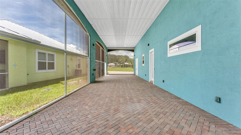 A covered patio with brick pavers, a screened wall, and bright blue exterior stucco walls — 3220 FISH HAWK DRIVE, POLK CITY, FL