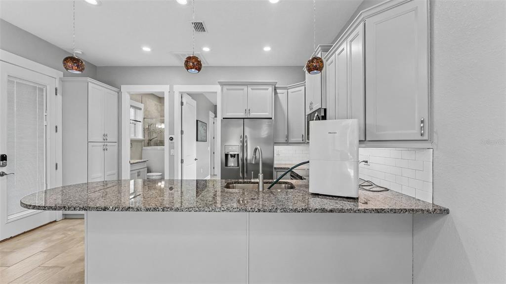 A kitchen features gray cabinets, granite countertops, a stainless steel refrigerator, and a kitchen island — 3220 FISH HAWK DRIVE, POLK CITY, FL