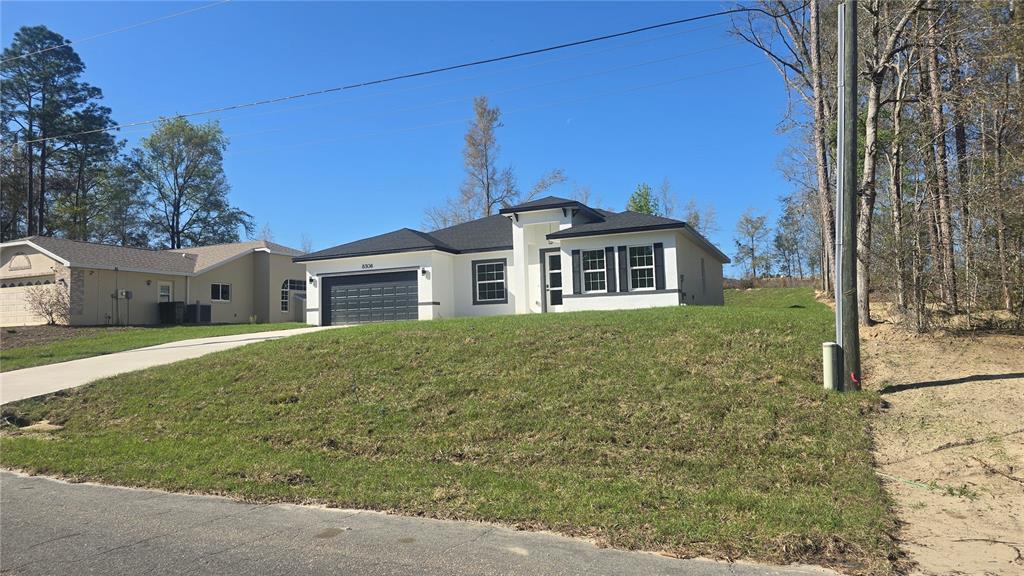A modern, single-story white house with a dark roof and garage sits on a grassy hill — 8308 N VINCE DRIVE, CITRUS SPRINGS, FL