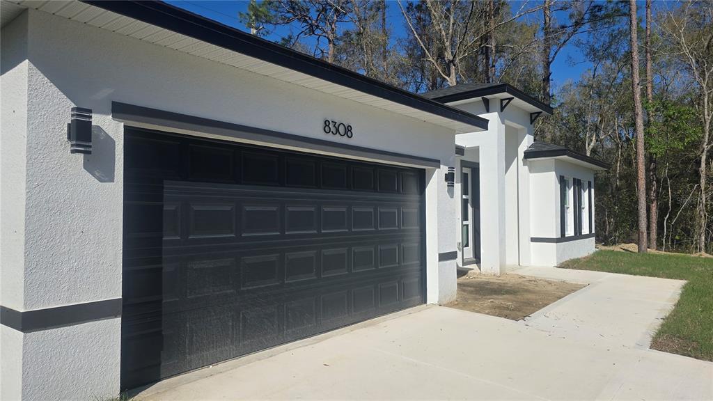 A modern white house exterior features a dark garage door and a concrete driveway — 8308 N VINCE DRIVE, CITRUS SPRINGS, FL