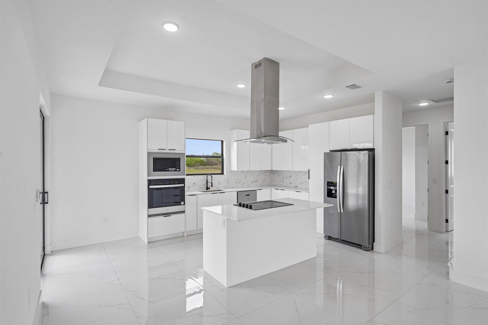 A modern white kitchen features stainless steel appliances, a center island, and marble-look tile flooring — 9035 W Broad Circle, FL 33935, FL