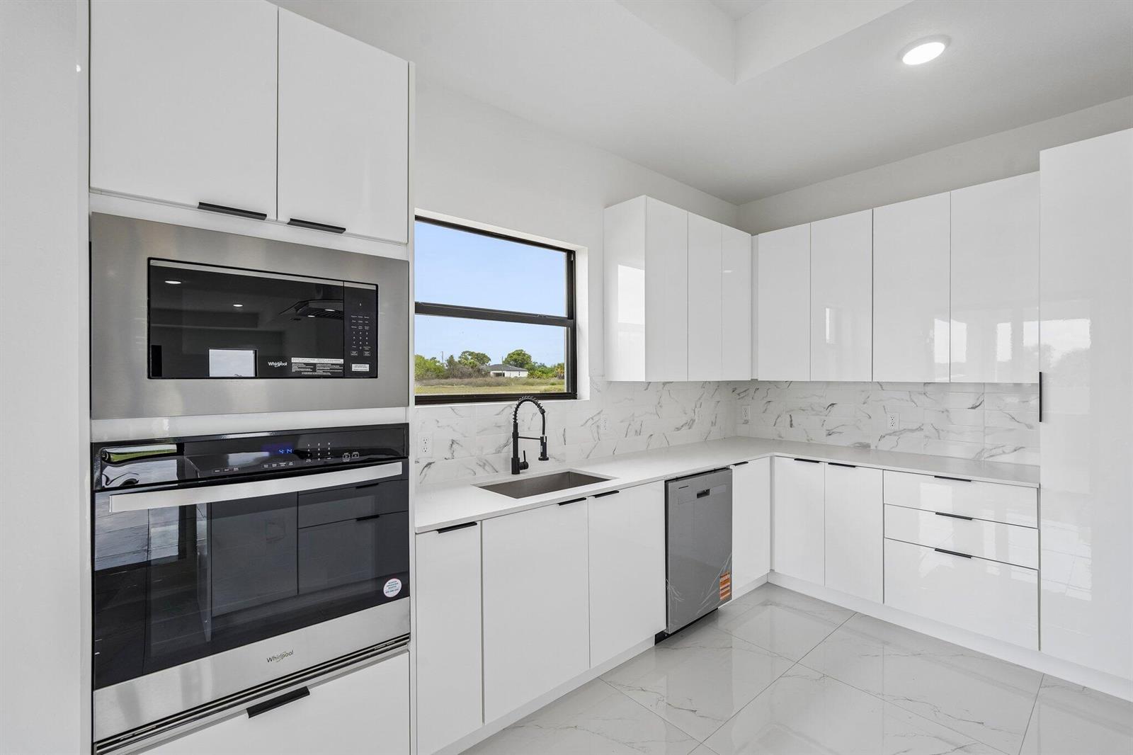 A modern kitchen features white high-gloss cabinets, stainless steel appliances, and marble-patterned tile backsplash — 9035 W Broad Circle, FL 33935, FL