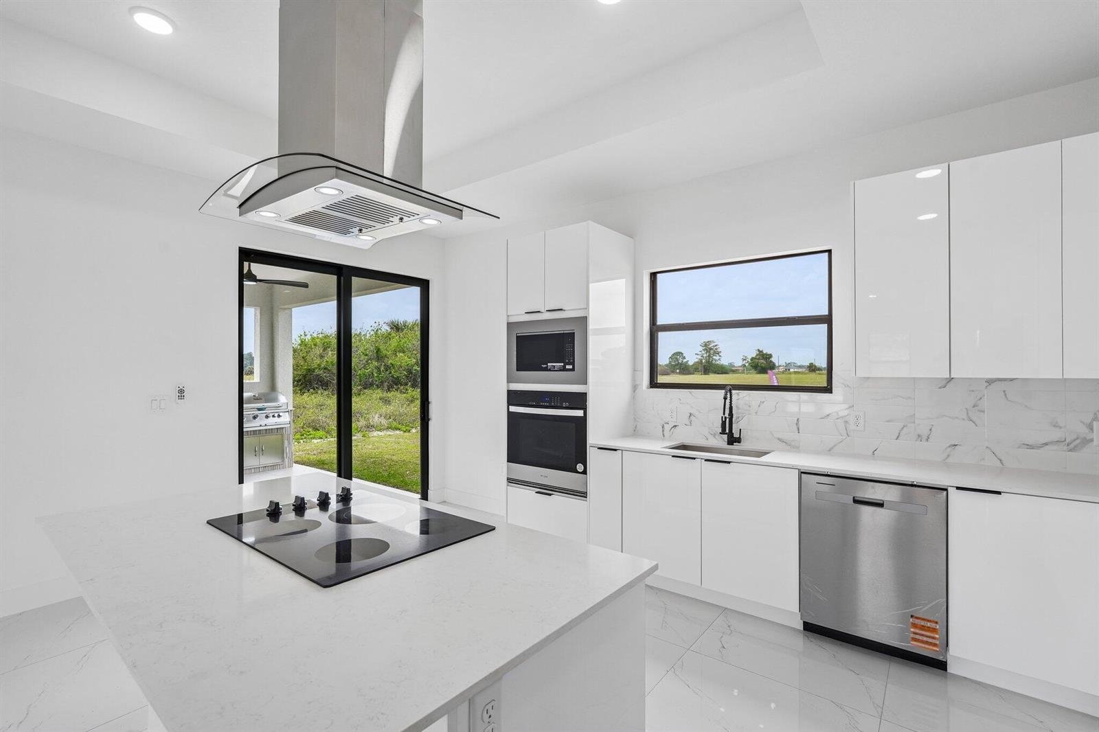 A modern white kitchen features a center island with a cooktop and stainless steel appliances — 9035 W Broad Circle, FL 33935, FL