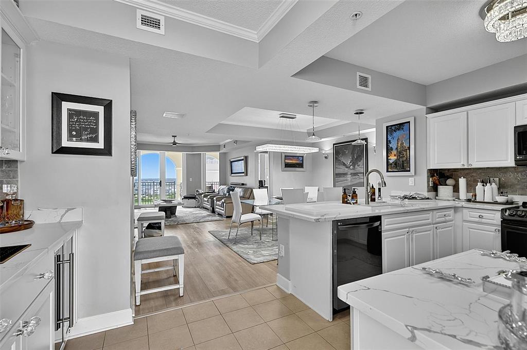 A modern kitchen with white cabinetry and marble countertops opens into a bright living area — 200 OCEAN CREST DRIVE UNIT 1018, PALM COAST, FL