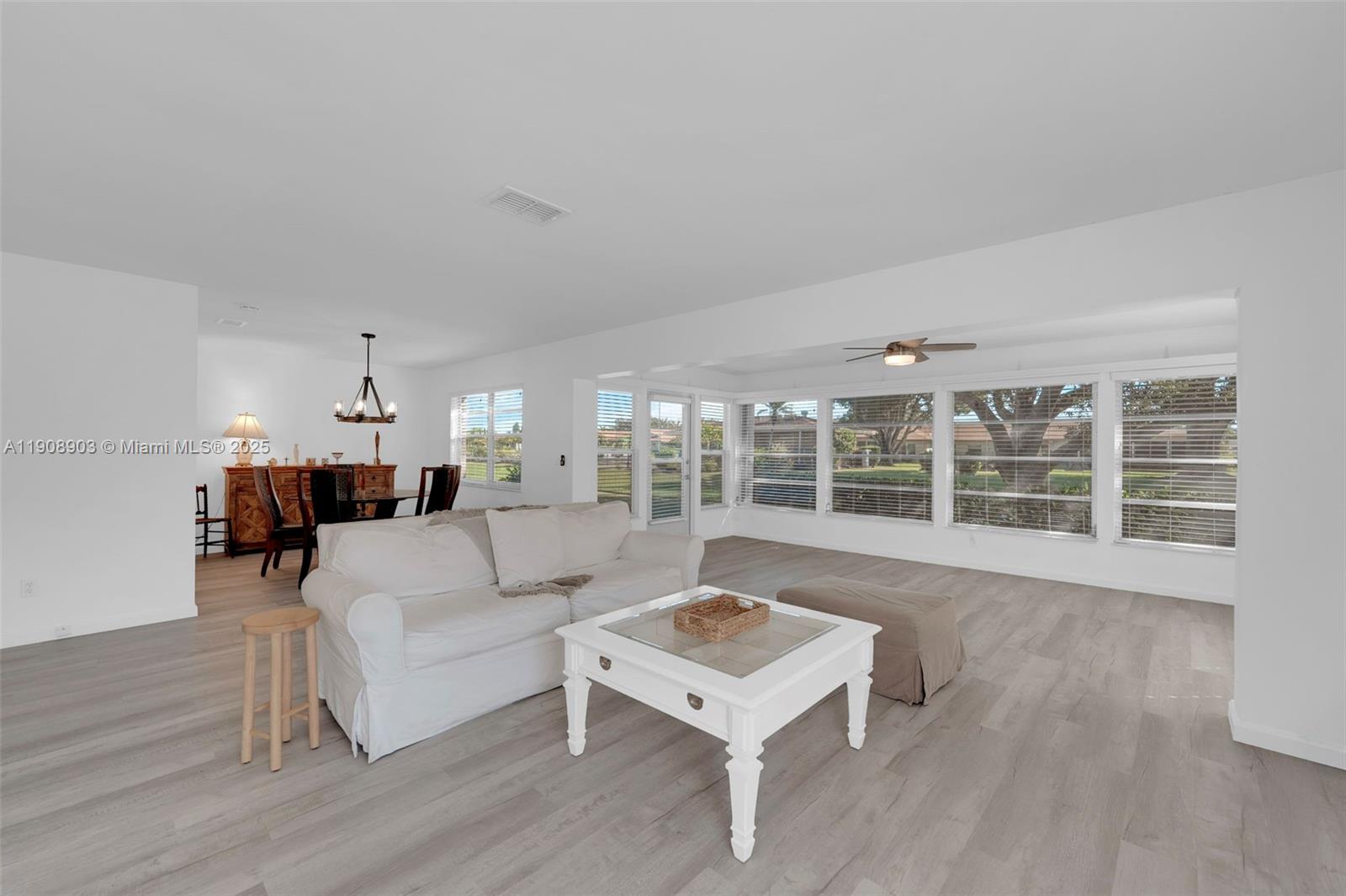 A living room features white walls, light wood-look flooring, a white sofa, and large windows — 5584 Buring Ct, Fort Myers FL 33919, FORT MYERS, FL