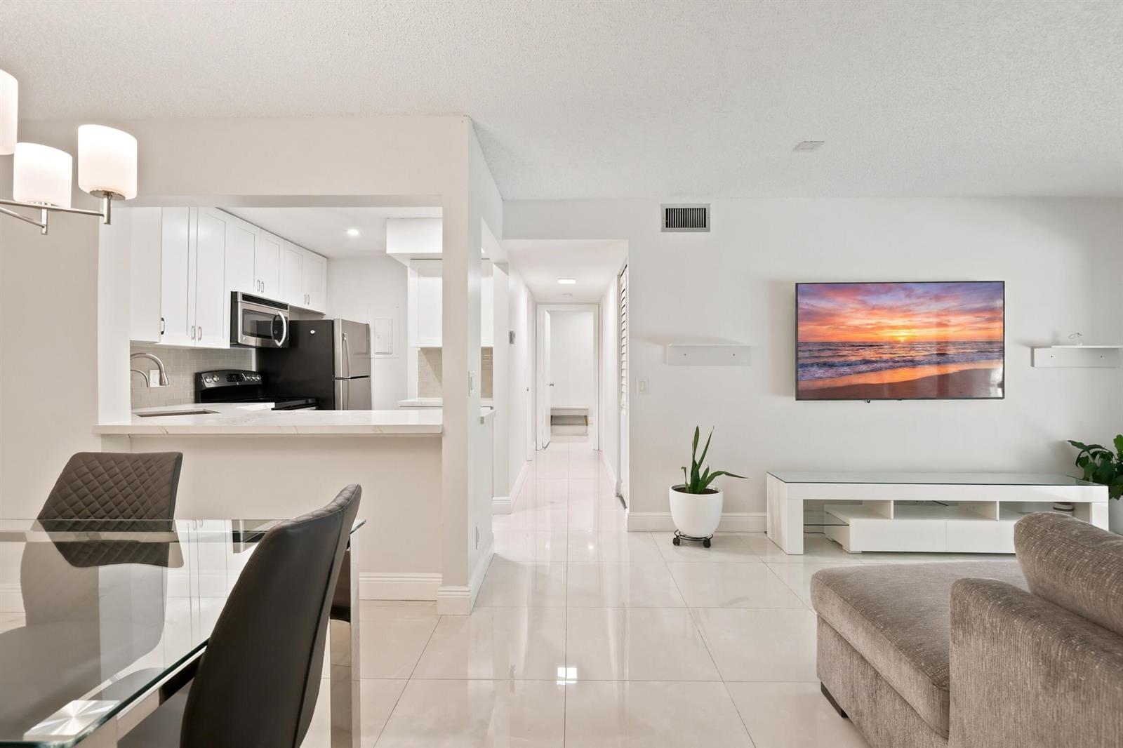 A bright living room and dining area with white tile floors and an open kitchen — 609 Sea Pine Way # F2, FL 33415, FL