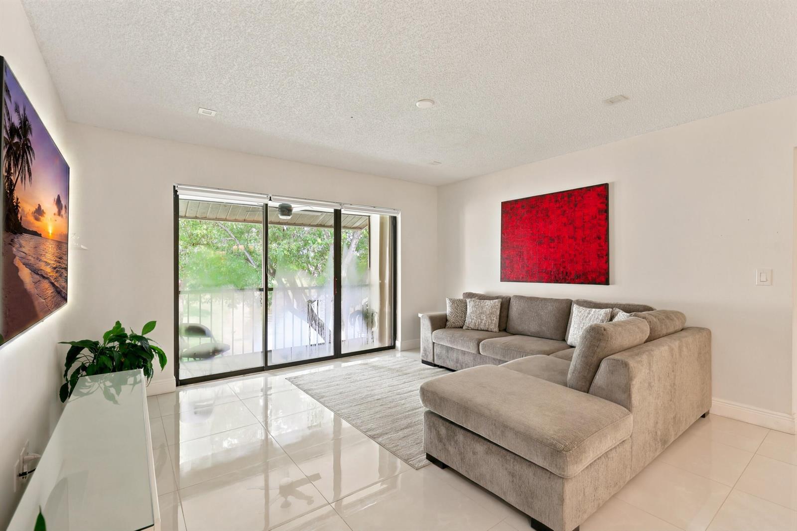 A living room features a gray sectional sofa, a red wall painting, and sliding glass doors — 609 Sea Pine Way # F2, FL 33415, FL