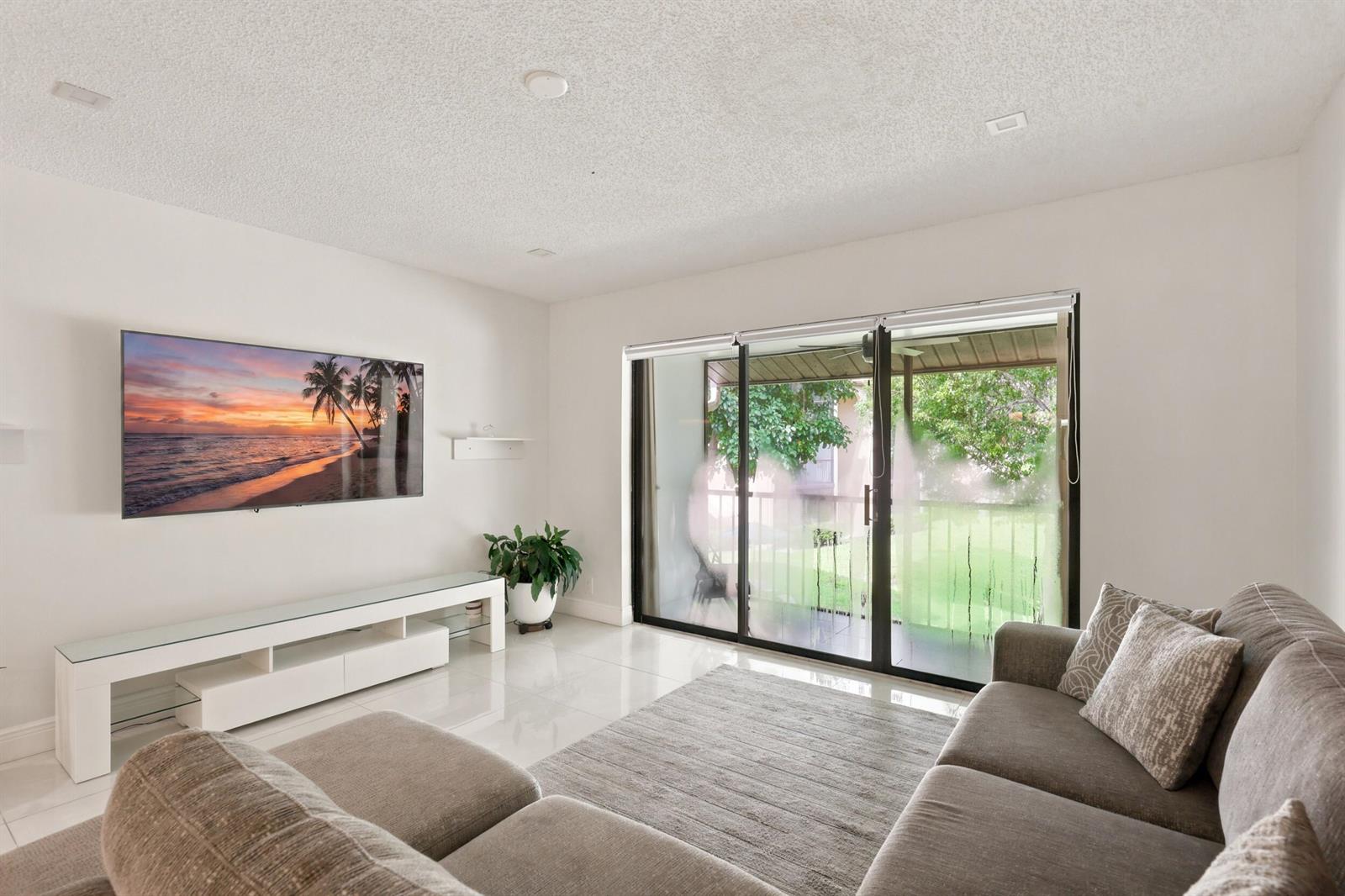 A living room features a wall-mounted television, white media console, tile flooring, and sliding glass doors — 609 Sea Pine Way # F2, FL 33415, FL