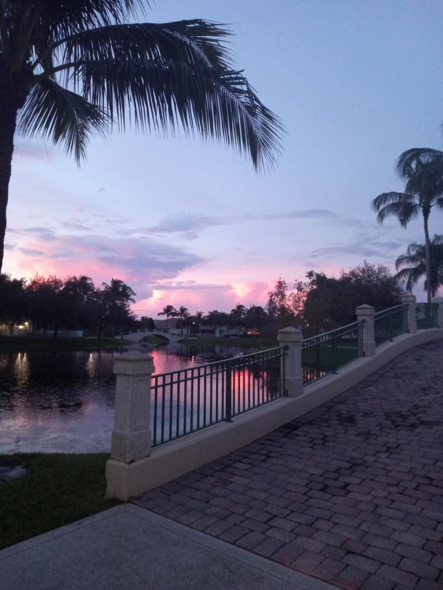 A brick walkway leads across a bridge overlooking a lake at sunset with palm trees — 8093 Montserrat Place, Wellington FL 33414, WELLINGTON, FL