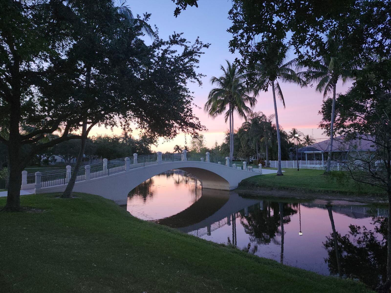 A white arched footbridge spans a calm canal at sunset surrounded by trees and grass — 8093 Montserrat Place, Wellington FL 33414, WELLINGTON, FL