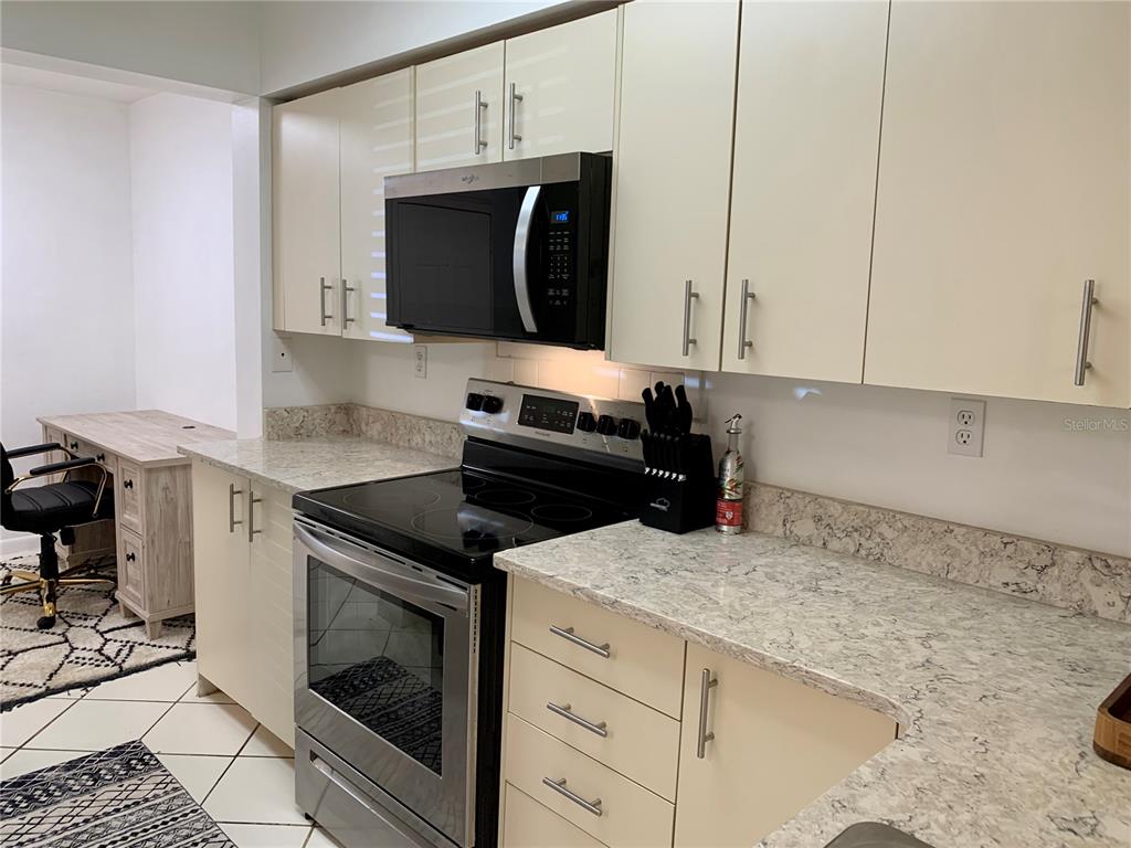 A kitchen features cream-colored cabinets, stainless steel appliances, and speckled stone countertops — 6061 BAHIA DEL MAR CIRCLE UNIT 146, ST PETERSBURG, FL