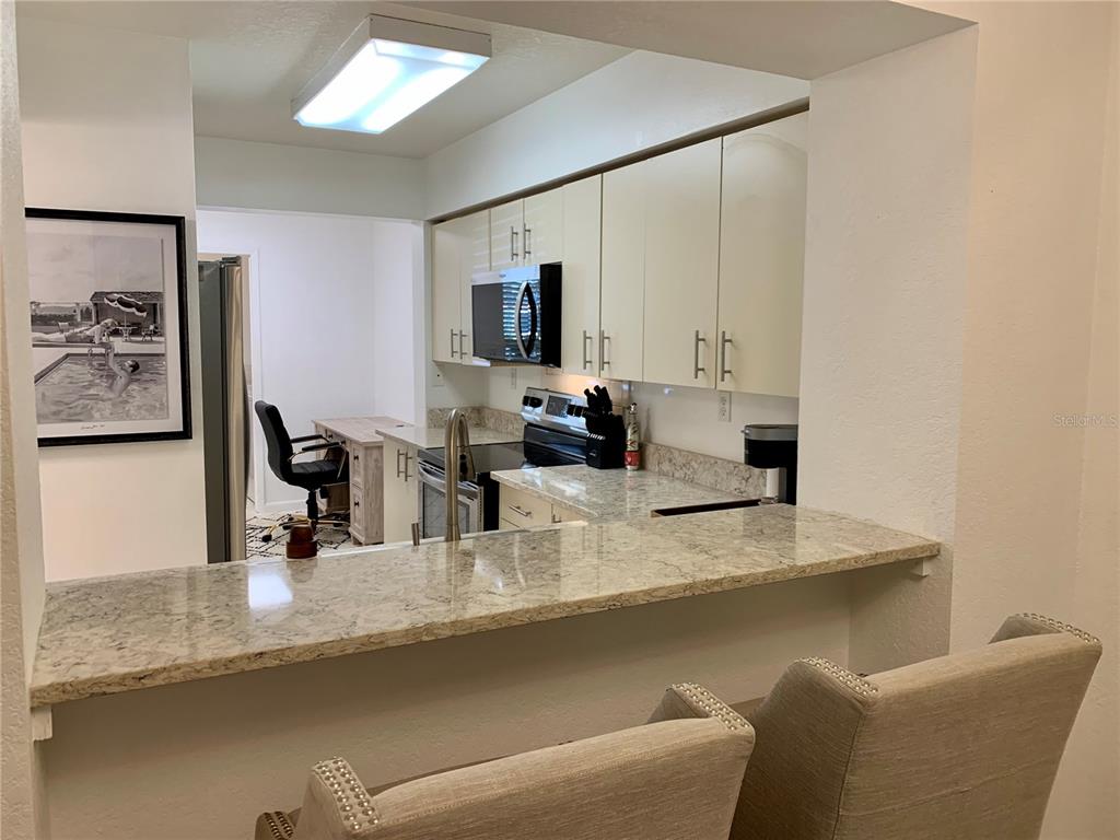 A kitchen with light-colored cabinets, granite countertops, and a breakfast bar with two chairs — 6061 BAHIA DEL MAR CIRCLE UNIT 146, ST PETERSBURG, FL