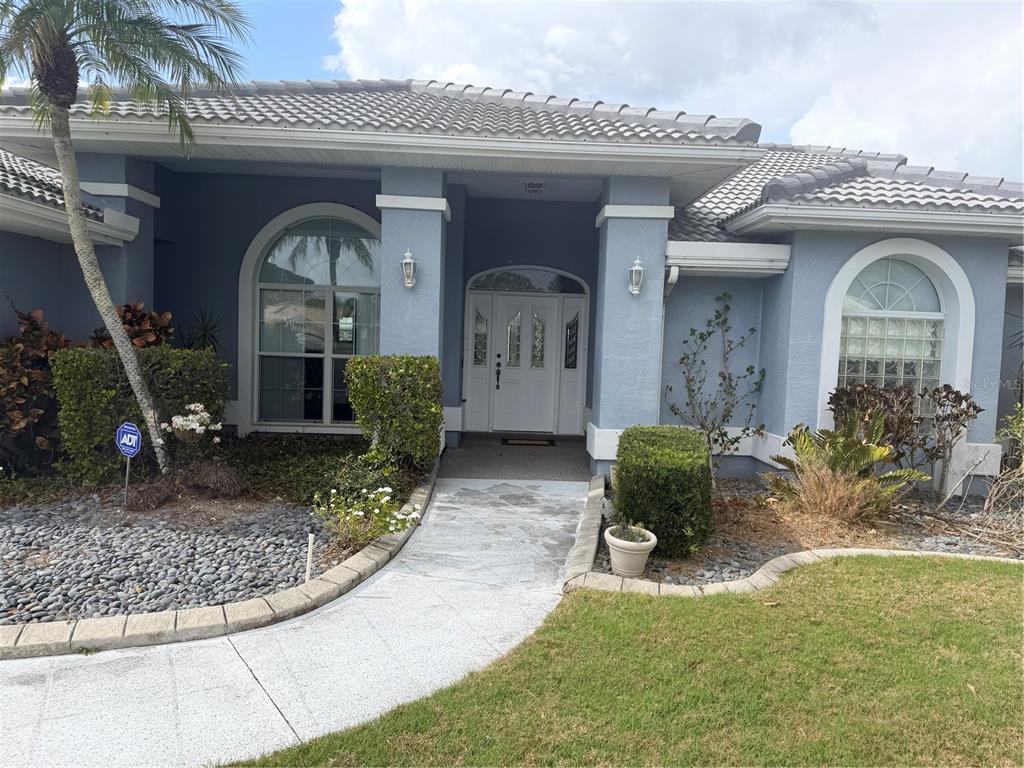 A blue single-story house with a white front door, arched windows, and a paved walkway — 6617 SEVEN PINES DRIVE, BRADENTON, FL