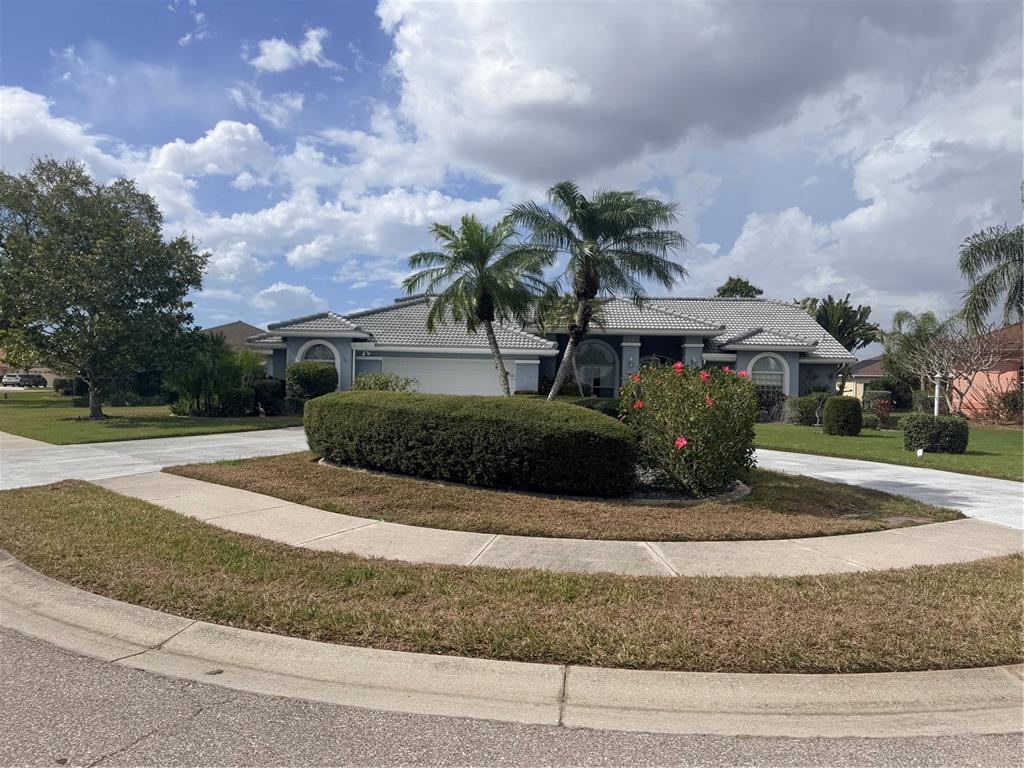A single-story house with a tiled roof, palm trees, and a landscaped circular driveway — 6617 SEVEN PINES DRIVE, BRADENTON, FL