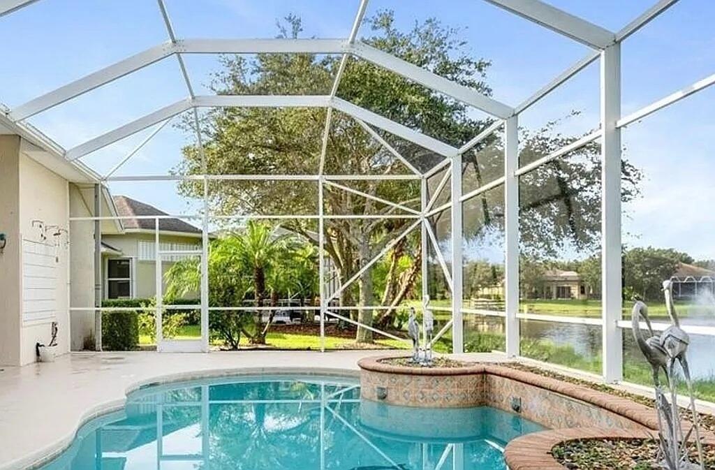 A screened-in pool enclosure features a curved spa, brick coping, and a view of a lake — 4204 Abington Woods Circle, Vero Beach FL 32967, VERO BEACH, FL